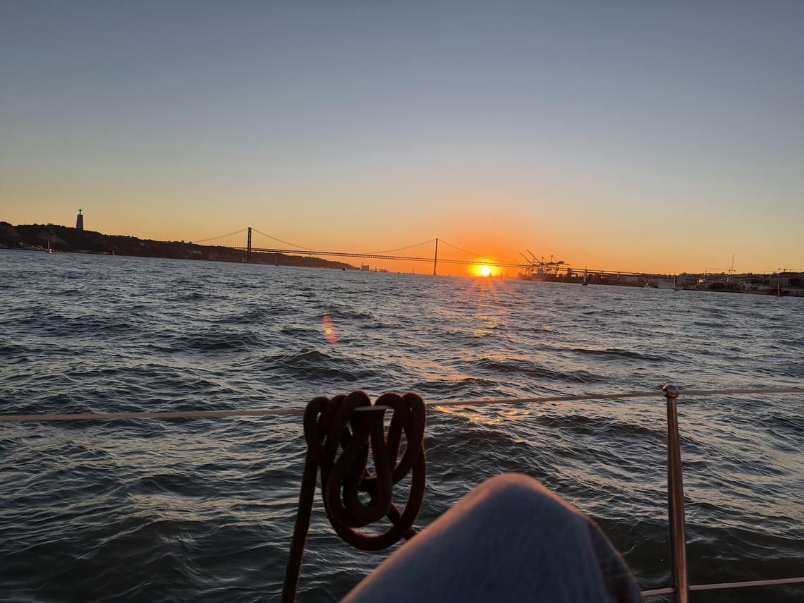 Sunset over the water, with a suspension bridge and harbor viewed from a sailboat.